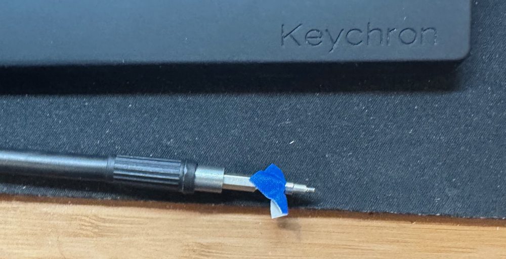 Blue painter's tape holding a tiny M.2 screw onto a long screwdriver bit.