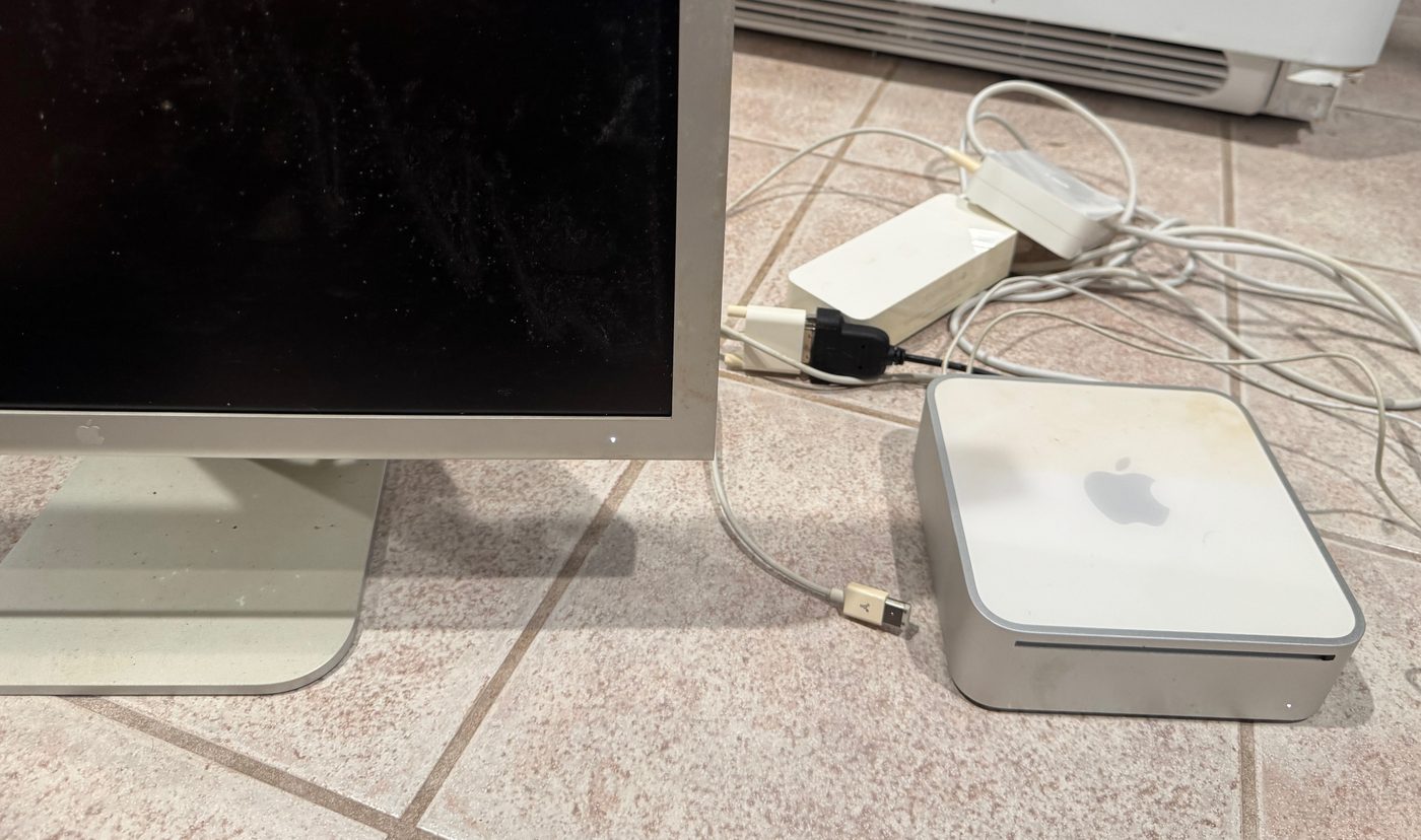 A 2009 Mac Mini and an Apple Cinema Display sitting on a tile floor with power bricks and cables